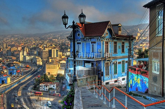 A tall blue timber house on the edge of a cerro, the port and its cranes far below