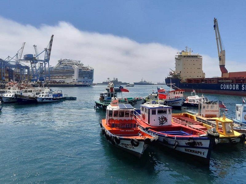Orange and white harbour launches tied up below the container cranes of Valparaiso port