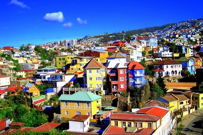 Brightly painted houses covering a Valparaiso hillside above the bay under a clear sky